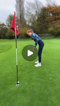 a woman hitting a golf ball on the green with a red flag in front of her