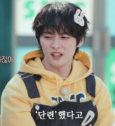 a young man wearing a yellow hoodie with an earphone in his hand and the caption says,