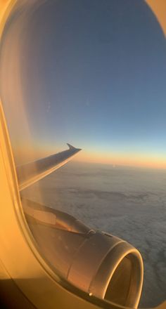 the wing of an airplane as seen from inside it's plane window, looking out over the clouds