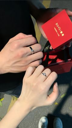 two people holding onto an engagement ring in a red box with the word love written on it