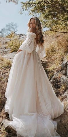 a woman in a white wedding dress standing on the side of a hill with trees