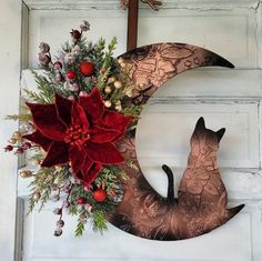 a christmas wreath with poinsettis and a cat on it hanging on a door