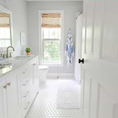 a white bathroom with hexagonal tile flooring and window above the toilet area