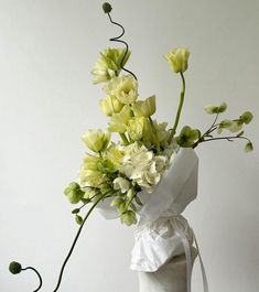 a bouquet of flowers in a vase on a white tablecloth with ribbon tied around it