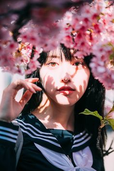 a woman with long black hair standing under pink flowers