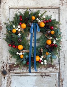 a wreath with oranges, berries and pine cones is hanging on an old door