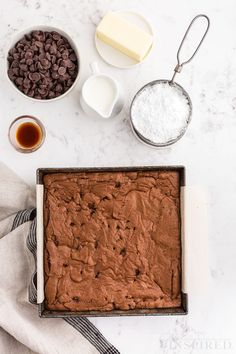 ingredients for chocolate cake laid out on a white counter top, including milk, sugar and butter