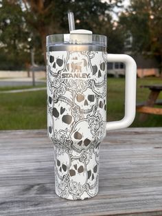 a white cup with skulls on it sitting on top of a wooden table next to a picnic table