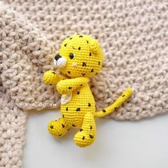 a crocheted yellow stuffed animal sitting on top of a white blanket next to a knitted sweater