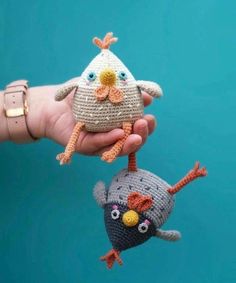 two crocheted birds are being held by someone's hand on a blue background