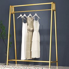 three dresses hanging on a clothes rack in front of a blue wall with white flowers