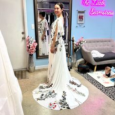 a woman standing in front of a mirror wearing a white dress with flowers on it