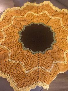 a yellow crocheted doily with a black center sits on top of a table