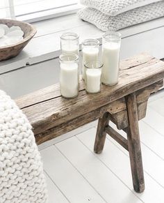 three candles sit on a wooden bench in front of a window with white pillows and blankets