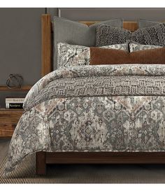 a bed with a gray and brown comforter on top of it next to a night stand