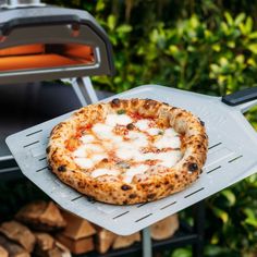 a pizza sitting on top of a metal rack next to a pile of firewood