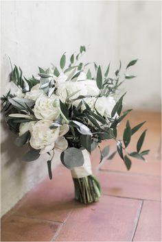 a bouquet of white flowers and greenery on the floor in front of a wall