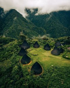 an aerial view of some huts in the middle of trees and grass with mountains in the background