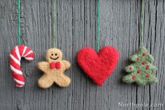 three felt christmas ornaments hanging on a wooden fence with candy canes and a gingerbread man