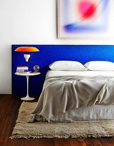 a bed with a blue headboard and white sheets in a bedroom next to a painting on the wall