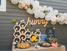 a dessert table with honeycombs, cupcakes and balloons on the wall