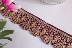 a purple and gold garter with flowers on the table in front of it, next to a glass vase