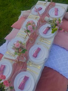 a table set up with pink and white plates, napkins and flowers on it