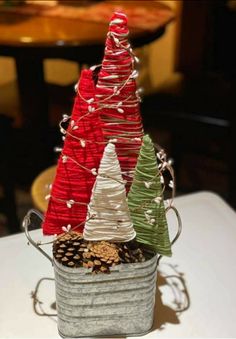 three small christmas trees sitting in a bucket on top of a table with pine cones