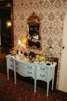 a table with many items on it in front of a mirror and wallpapered walls