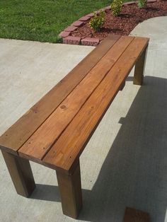 a wooden bench sitting on the side of a sidewalk next to a flower bed and grass