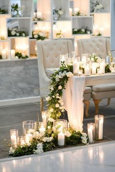 a table with candles, flowers and greenery on it in front of some chairs