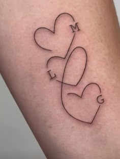 a small tattoo on the leg of a woman with two hearts and a letter m