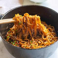 the noodles are being stirred with chopsticks in the skillet on the table