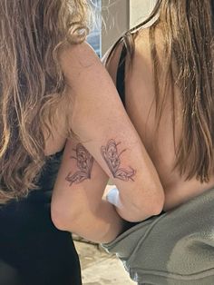 two women with tattoos on their arms looking at each other's reflection in a mirror