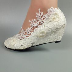 a woman's white wedding shoe with lace and pearls on the heel, decorated with flowers