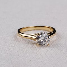 a yellow gold ring with a single diamond on the top, sitting on a white surface