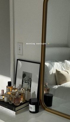 a mirror sitting on top of a white counter next to bottles and perfumes in front of a bed