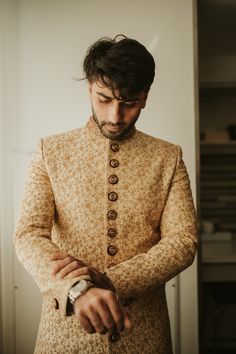 a man standing in front of a white wall wearing a brown and tan suit with buttons on it