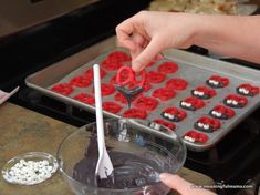 someone is decorating cupcakes with red and white icing on the tray