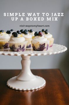 cupcakes with white frosting and blueberries sitting on a cake platter