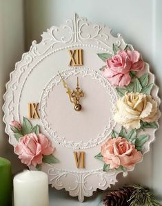 a white clock with flowers on it next to a candle and some pineconi