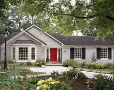 a white house with red front door and black shutters on the windows is surrounded by greenery