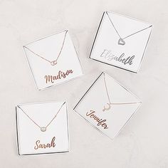 four personalized necklaces in boxes on a white surface with the names of three different people