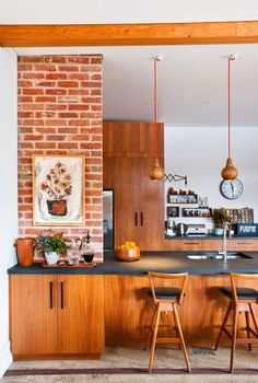 a kitchen with wooden cabinets and black counter tops next to a brick wall that has hanging lights above it