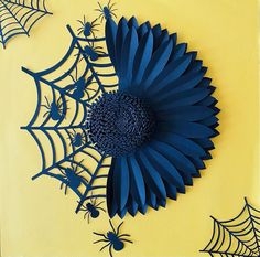 blue paper flowers and spider webs are on a yellow background with black widowes