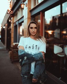 a woman standing in front of a building with her arms crossed and looking at the camera