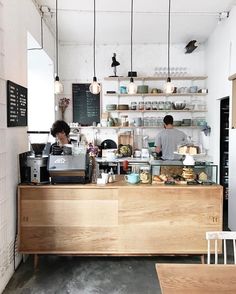 two people working behind the counter in a coffee shop with shelves and hanging lights above them