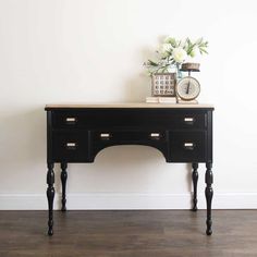 a black desk with two drawers and a clock on top, against a white wall