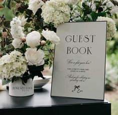 a vase with white flowers sitting on top of a table next to a sign that says guest book