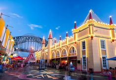 an amusement park at night with lights on the building and people walking around it in front